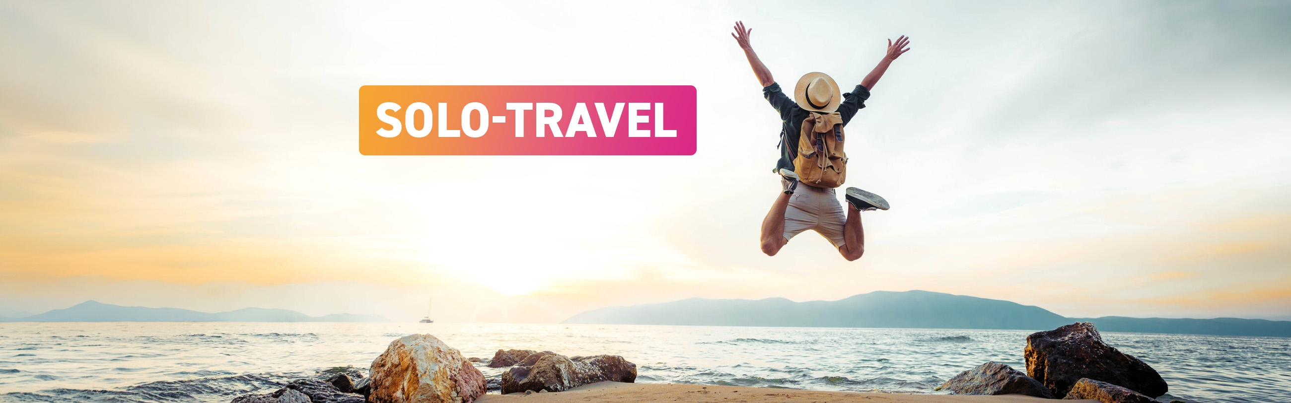 Mann mit Rucksack springt am Strand vor dem Meer in die Luft und streckt die Arme nach oben